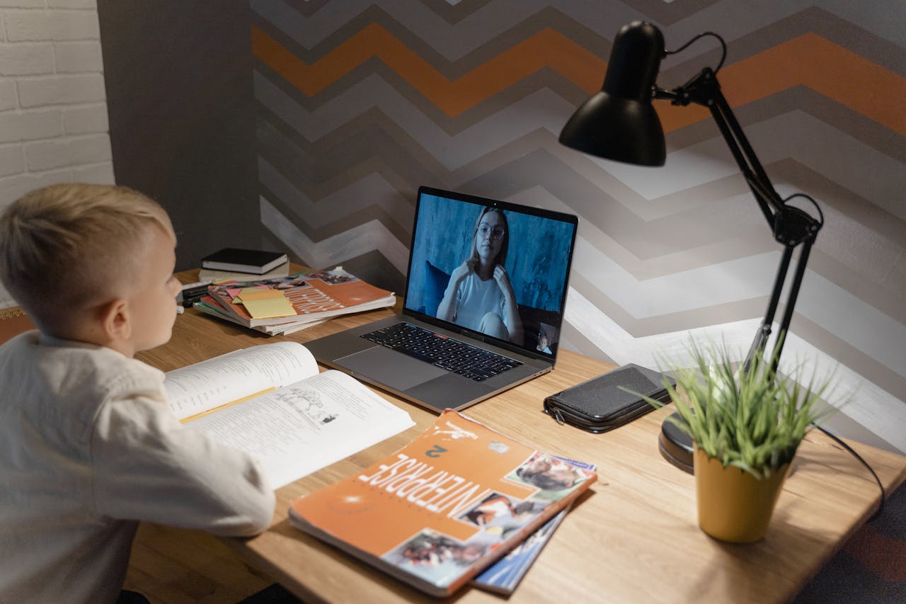 our-story A young boy participates in a virtual class from home, using a laptop and study materials.
